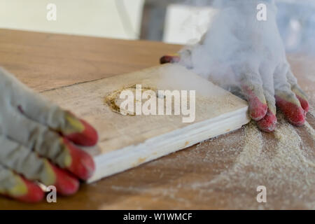 Hands of the master in gloves hold a wooden billet, while working on the milling equipment Stock Photo