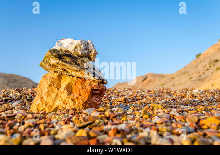 Stones, pebbles & seashells stuck on stone near the beach with clear blue sky. Low angle view from Muscat, Oman. Stock Photo