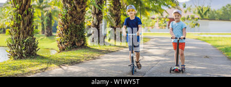 BANNER, LONG FORMAT Boy and girl on kick scooters in park. Kids learn to skate roller board. Little boy skating on sunny summer day. Outdoor activity Stock Photo