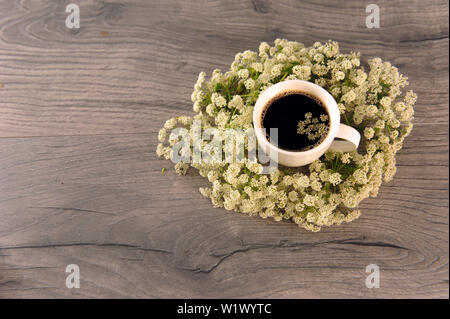 High angle view of coffee in white cup surrounded by white flowers on grey wooden surface. Cowparsley and hot beverage. Horizontal photo with copy spa Stock Photo