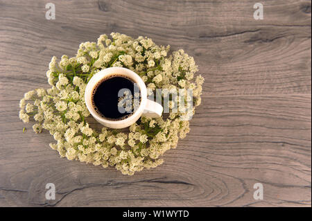 White cup of coffee on grey wooden table surrounded by white cowparsley flowers.  Horizontal photo with copy space to the right. Stock Photo