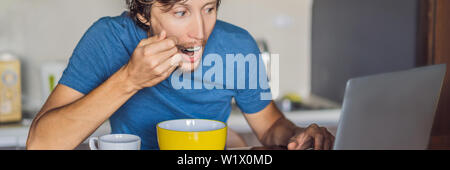 Young man having breakfast and using laptop on the kitchen BANNER, LONG FORMAT Stock Photo