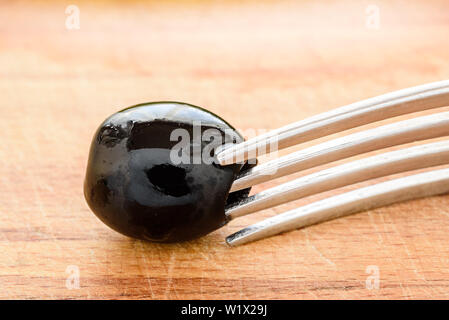 One Berry black olives on fork, close-up Stock Photo