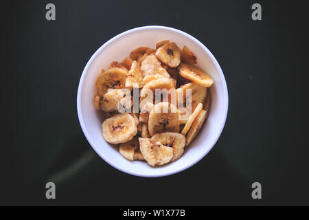 Dried bananas in the white bowl on the black background taken from the top. Stock Photo