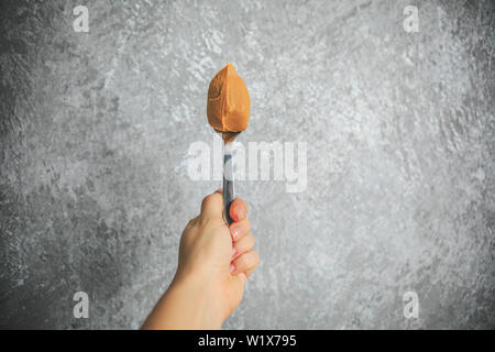 Peanut butter on the spoon holding in hand on the gray and white background. Stock Photo