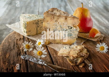 A slice of blue aged Stilton cheese on a wooden table. Cheese is served with a beautiful ripe pear. The quality of farmers ' agricultural products. De Stock Photo