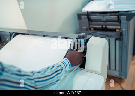 Modern printing technique. Close up of dark-skinned man wearing striped shirt using big modern printing technique Stock Photo