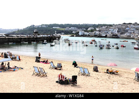 St. Ives, Cornwall, UK. June 25, 2019. Holidaymakers enjoying the sands of the harbor beach with a glorious view of the town and harbor at St. Ives in Stock Photo