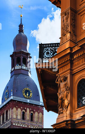 Buildings of the city exchange in Riga with a bas-relief and a balcony against the background of the Dome Cathedral with a golden cockerel on a spire Stock Photo