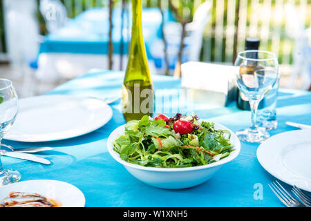 Greek, Mediterranean or Aegean Green fresh vegetarian Salad on the table in Fish Restaurant. Green Salad in bowl with olive oil at Beach Restaurant Stock Photo
