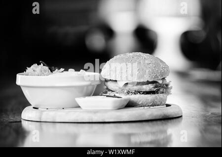 High calorie snack. Hamburger and french fries and tomato sauce on wooden board. Fast food concept. Burger with cheese meat and salad. Cheat meal. Delicious burger with sesame seeds. Burger menu. Stock Photo