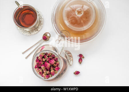 Tea made from rosebuds . Tea rose buds made from real rose buds, plucked young and then dried. A Cup of tea and a transparent teapot with a beautiful Stock Photo