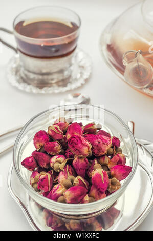 Tea made from rosebuds . Tea rose buds made from real rose buds, plucked young and then dried. A Cup of tea and a transparent teapot with a beautiful Stock Photo