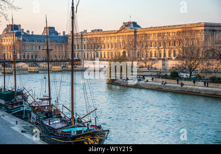 View of the Louvre Museum and palace from the banks of the Seine River with sailing ships in the foreground with the afternoon light. Stock Photo