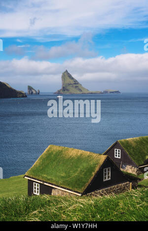 Houses on the coast of Faroe Islands with Drangarnir sea stack in the background Stock Photo