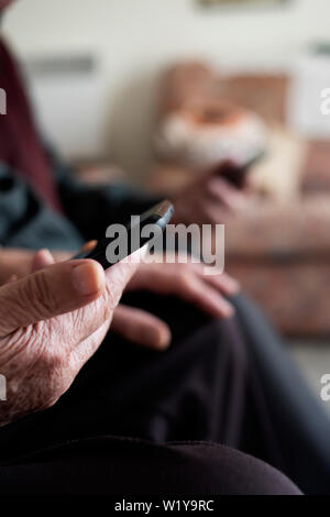 closeup of an old caucasian woman and an old caucasian man using their smartphones, sitting in a couch Stock Photo