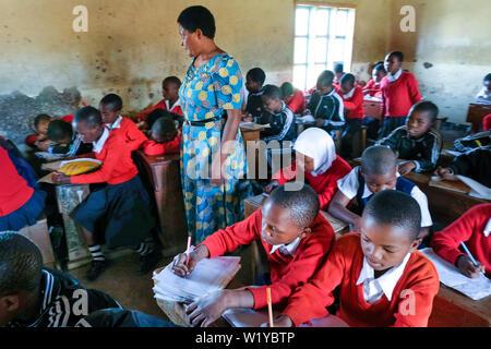 Teacher and students in red school uniforms in a school class of the Mwenge Primary School in Mbeya, Tanzania