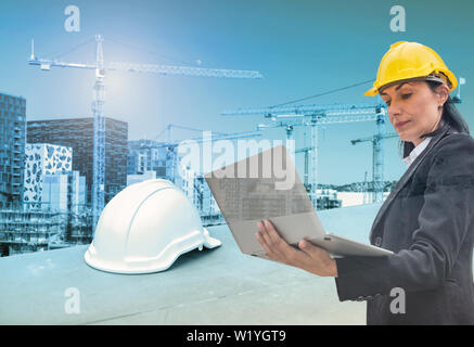 Woman engineer holding laptop with helmet on construction building with cranes background Stock Photo