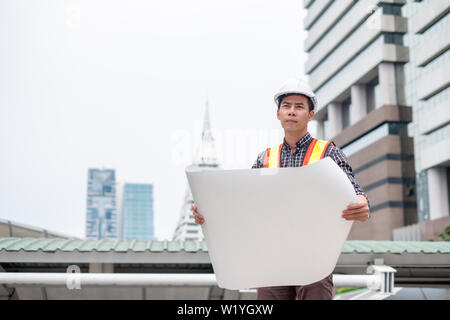 Man engineer standing open blueprint with looking be concentrated in the city Stock Photo