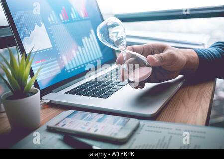 Business concepts with businessman holding hourglass with graph chart on computer laptop.For investment analysis,Waiting to sucess ideas Stock Photo