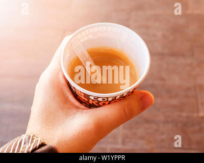 Woman hand holding a cardboard cup with coffee. Hot coffee from outdoors vending coffee machine. Close-up. Top view. Stock Photo