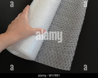 Woman hand holding white transparent bubble wrap roll for packaging fragile items on black background, close up. Stock Photo