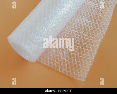 Transparent bubble wrap roll for packaging fragile items on yellow background. Top view, close-up. Stock Photo
