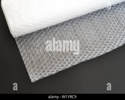Transparent bubble wrap roll for packaging fragile items on black background. Top view, close up. Stock Photo