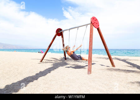 middle aged woman swinging on a swing. On the beach with the sun on her face in Spain.