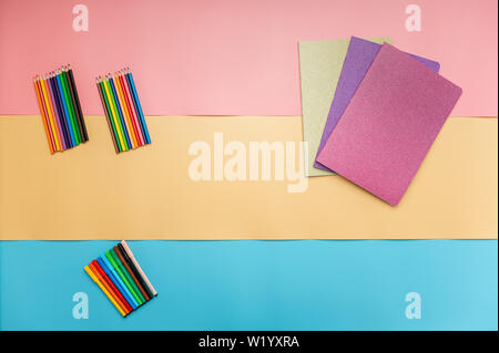 Shiny notebooks, colour pencils and colouring pens on a colourful paper background in a back to school conceptual image. Stock Photo
