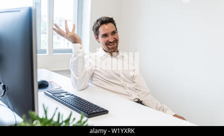 Cheerful businessman sitting at his office desk with computer explaining something. Stock Photo