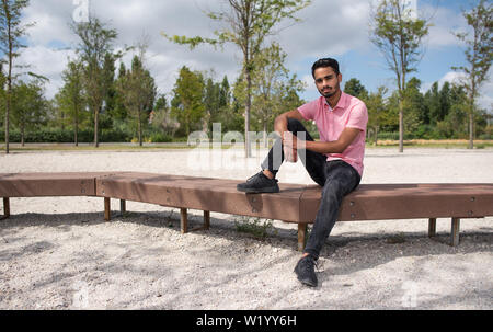 young male model sitting in a bench in a garden Stock Photo