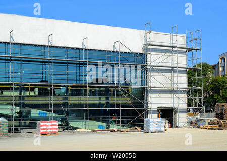 Construction of modern shopping mall against the blue sky on a sunny autumn day. Its facade of glass and concrete surrounded by scaffoldin. Stock Photo