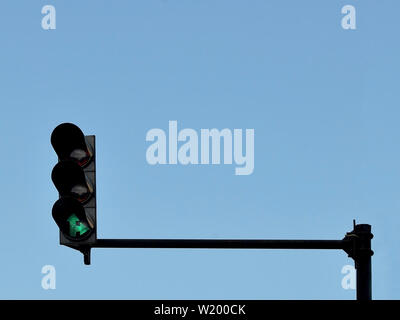 Green traffic light installed on a pole above a roadway, against a blue sky, copy space Stock Photo