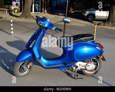 Bright blue colored scooter parked on the street on a summer day close-up. Stock Photo