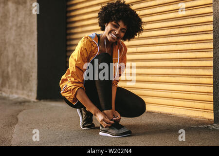 Smiling african woman in fitness wear tying her shoelace. Fitness woman tightening her shoes during workout. Stock Photo