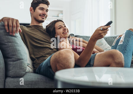 Lovely young couple relaxing at home enjoying a television program. Man and woman relaxing on sofa watching television together at home. Stock Photo