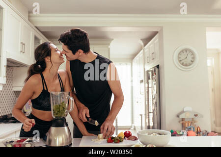 Fit young couple in love preparing healthy smoothie in kitchen. Couple about to kiss while preparing healthy breakfast in kitchen. Stock Photo