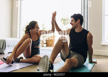 Couple giving each other high five after a successful workout together. Man and woman in sports wear doing workout in living room. Stock Photo