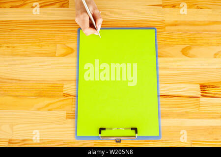 Office Hand Holding a Folder with a Green Color Paper on the Background of the Wooden Table. Copyspace. Place for Text Stock Photo
