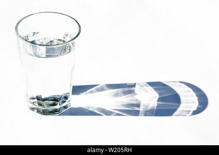Glass beaker from which padajet sharp shadow, stands on a white background. Empty space for text Stock Photo