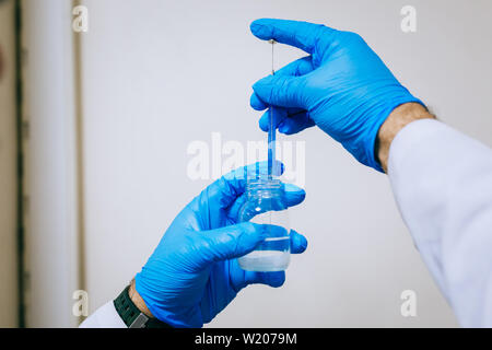 Man or male hands in protective gloves hold test tube in hands produces chemistry experiment test and research in modern chemistry lab. Chemist Stock Photo