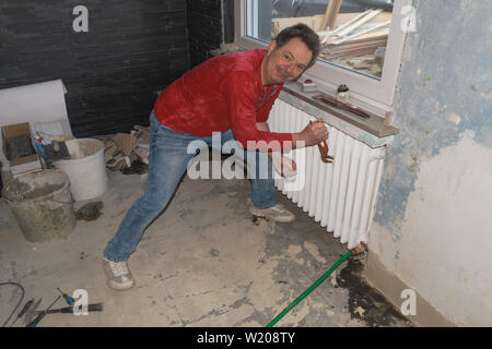 Plumber or installer disassembling an old finned tube heater Stock Photo