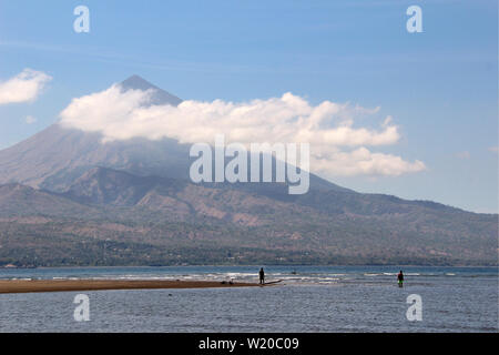 Fishers in the water of a lake in front of a high volcano with clouds in Sulawesi, Indonesia. Stock Photo