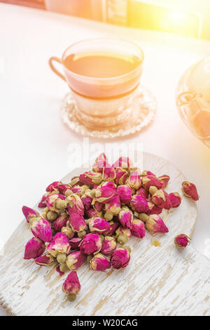 Tea made from rosebuds . Tea rose buds made from real rose buds, plucked young and then dried. A Cup of tea and a transparent teapot with a beautiful Stock Photo