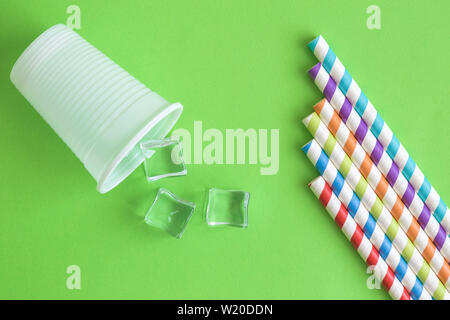 Flat lay of disposable cup with ice cubes and colorful drinking straws against green background minimal drink refreshment summer creative concept. Stock Photo