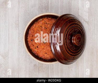 A ceramic pot of traditional Eastern European stewed cabbage on a white wooden kitchen board. Stock Photo