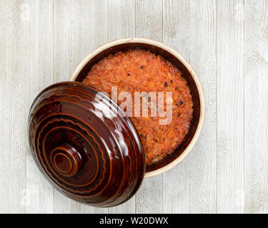 A ceramic pot of traditional Eastern European stewed cabbage on a white wooden kitchen board. Stock Photo