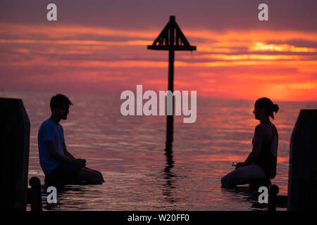 Aberystwyth Wales UK, Thursday 04 July 2019  UK Weather: A young couple are silhouetted against the sky as they balance on the wooden jetty  in the flat calm sea and watch the glorious sunset in Aberystwyth on the Cardigan Bay coast, west Wales.   photo credit: Keith Morris//Alamy Live News Stock Photo