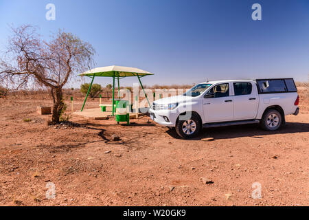 Toyota Hilux pick-up truck stopped beside a concrete picnic table and benches with a canopy for shade, typically placed every 10-20kms along roads in Stock Photo